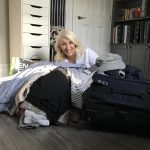 Jayne sitting on floor smiling with clothes for packing for her lone traveller trip