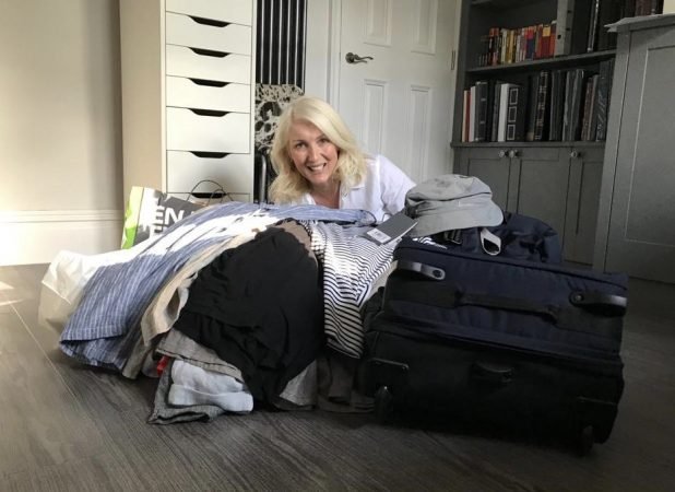 Jayne sitting on floor smiling with clothes for packing for her lone traveller trip