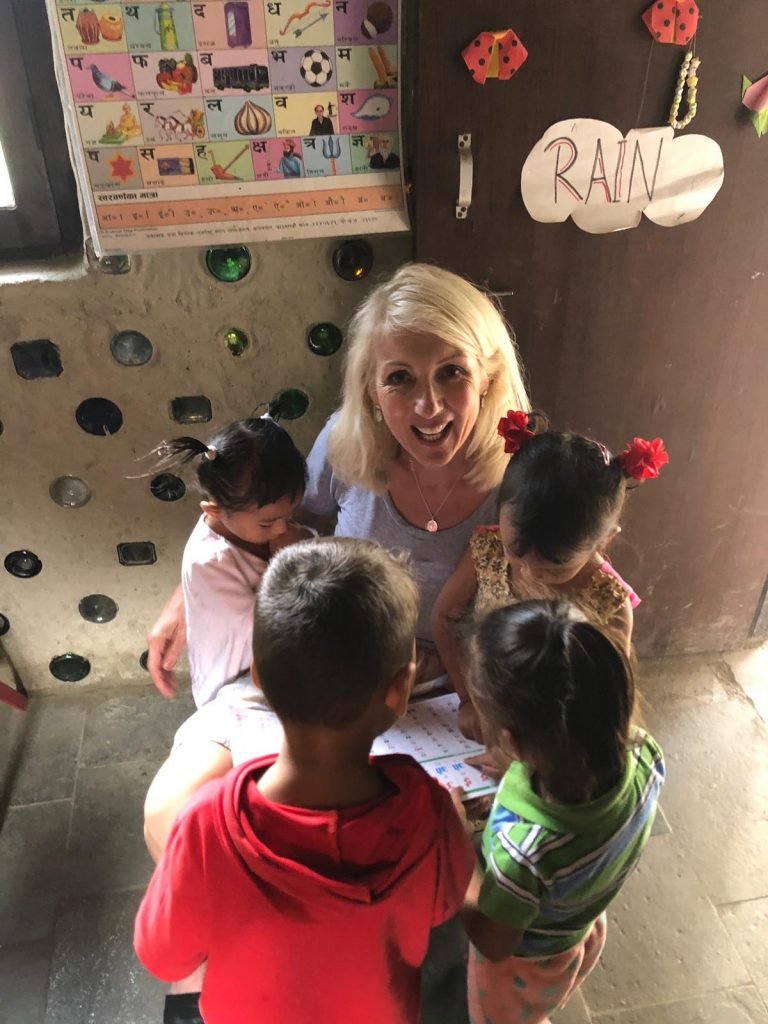 Jayne smiling, surrounded by school children whilst volunteering in Nepal